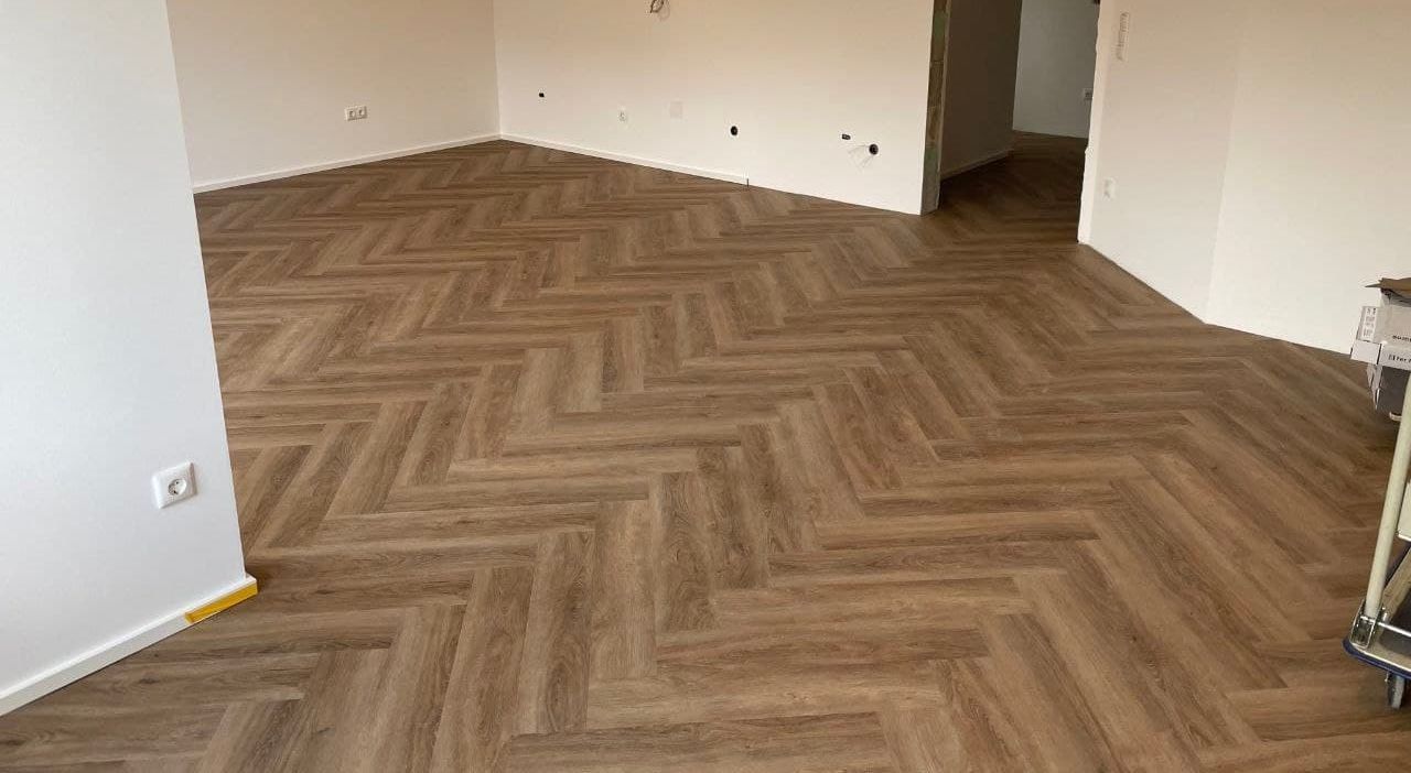 Leerer Wohnraum, tief fotografiert, mit fertig verlegtem Designboden im Fischgrätmuster bis in die Türöffnung